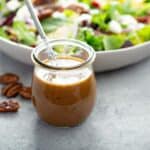 A glass container of homemade balsamic vinaigrette dressing beside a fresh salad sprinkled with pecans, showcasing a classic dressing with a Southern twist.