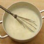 sauce pan containing white sauce and a whisk